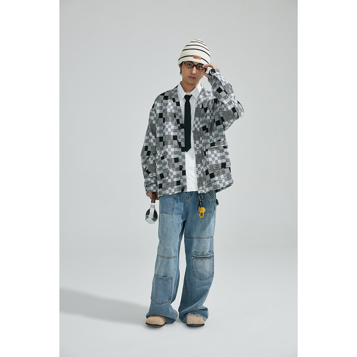 Model wearing a black, gray and white patchwork-check cardigan with blue jeans, a striped beanie and glasses.