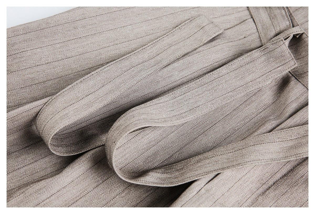 Close-up of taupe-gray herringbone trouser fabric and a curved folded waistband or belt detail.
