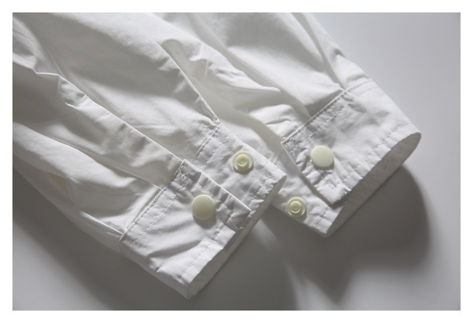 Close-up of two white shirt cuffs with large pale buttons and smaller matching fasteners.