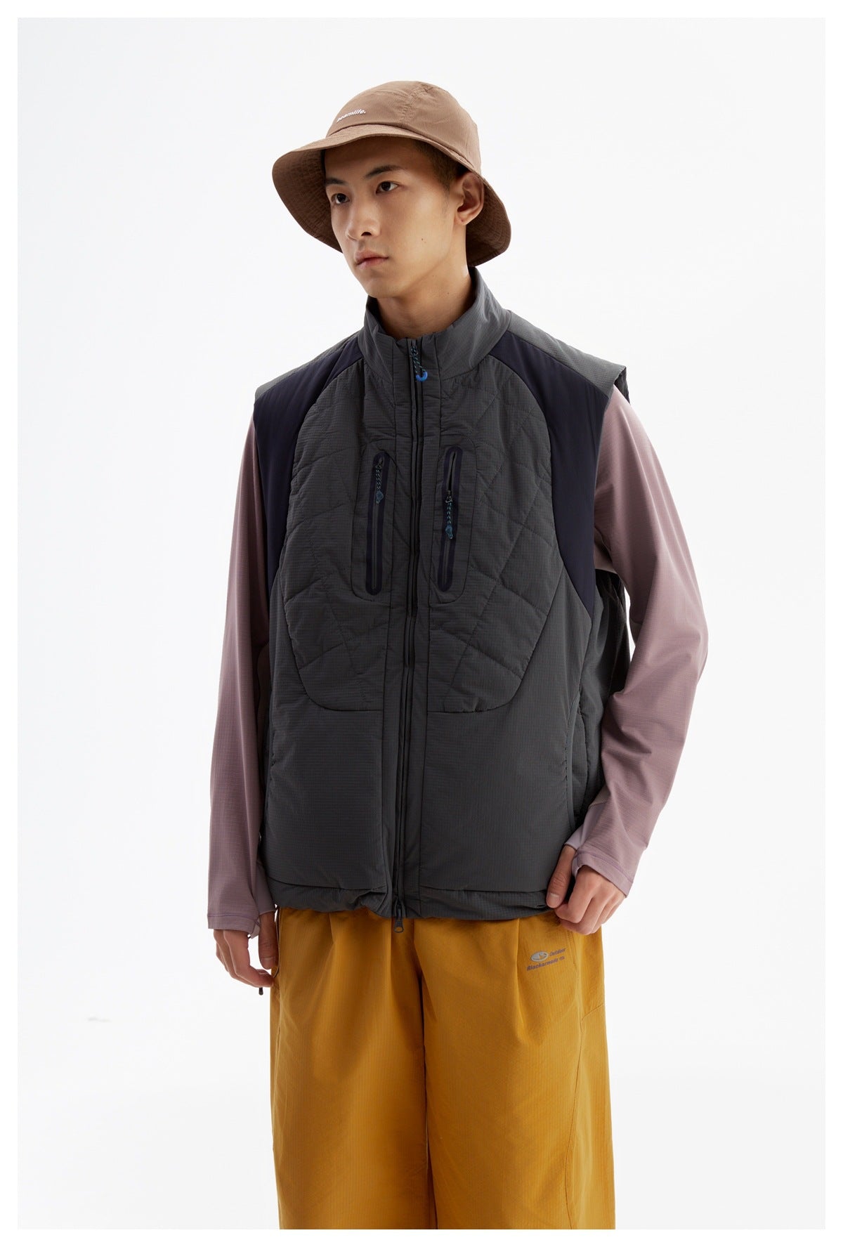 Close view of a model wearing a charcoal quilted vest with a high collar, front zip, and two vertical chest pockets.