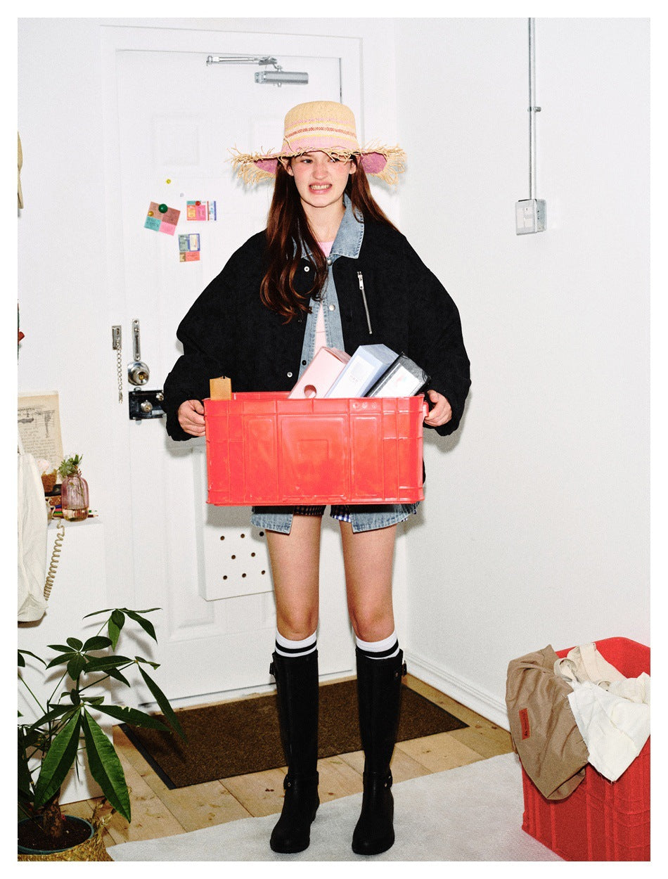 Model wearing a black jacket with denim trim while holding a red crate in front of the lower outfit.