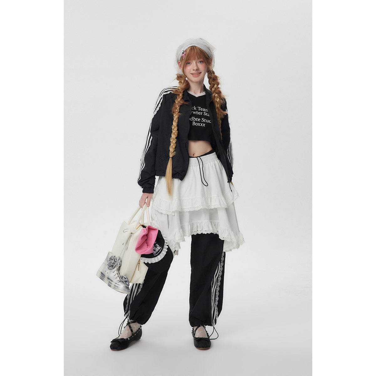 Full-length model wearing a black jacket with white sleeve stripes, a white tiered lace skirt and black track pants.