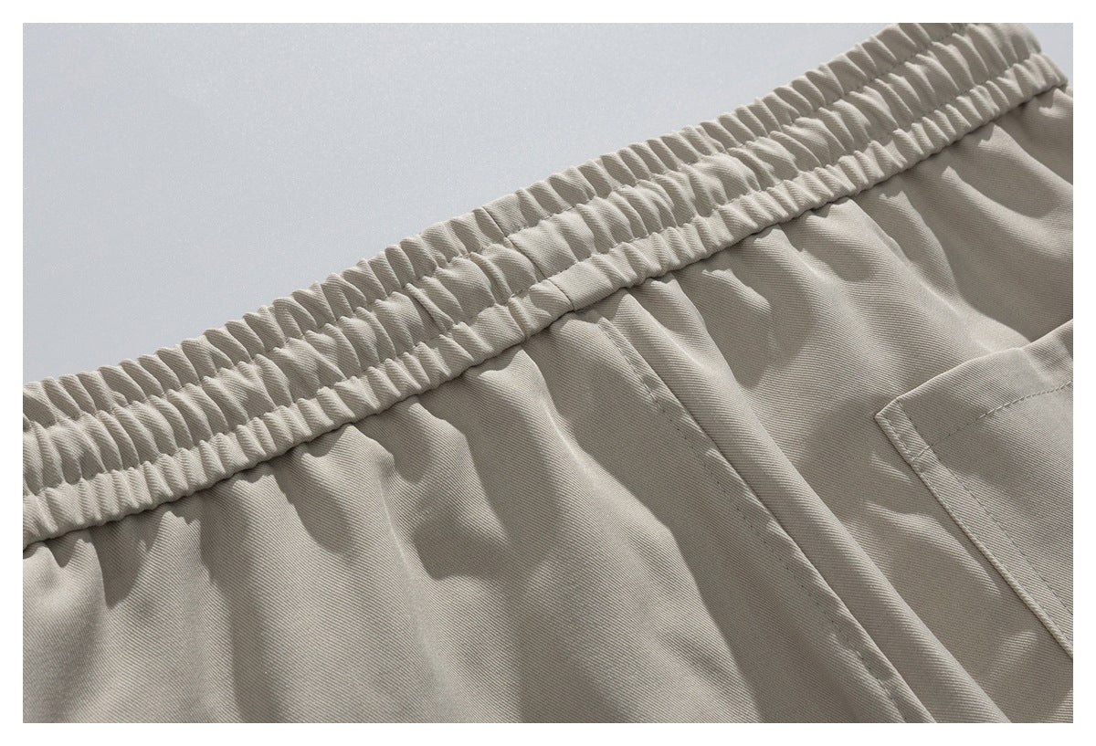 Close-up of light beige trousers showing the gathered elastic waistband, stitching, and edge of a pocket.