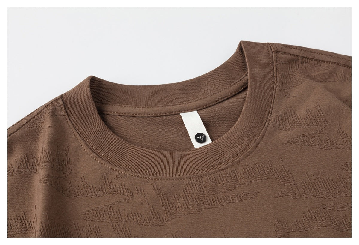 Close-up of a brown crew-neck T-shirt showing its ribbed collar, textured pattern and size tag.