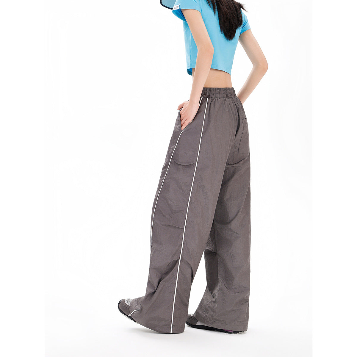 Rear three-quarter view of a model wearing charcoal gray wide-leg pants with white side piping and an elastic waist.