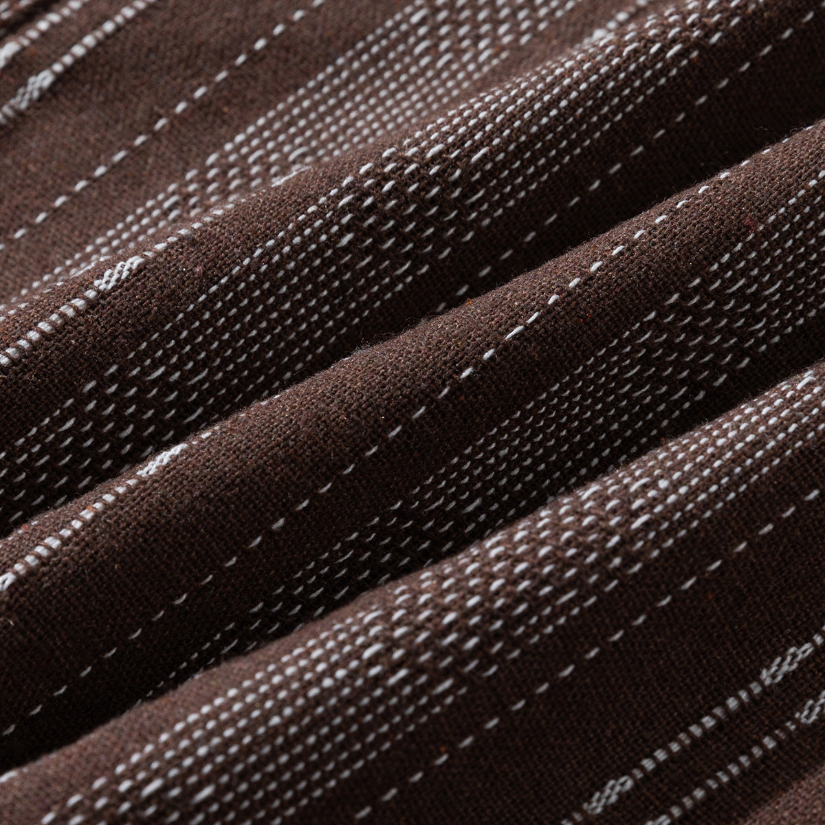 Macro view of brown fabric with irregular white woven stripes and folds.