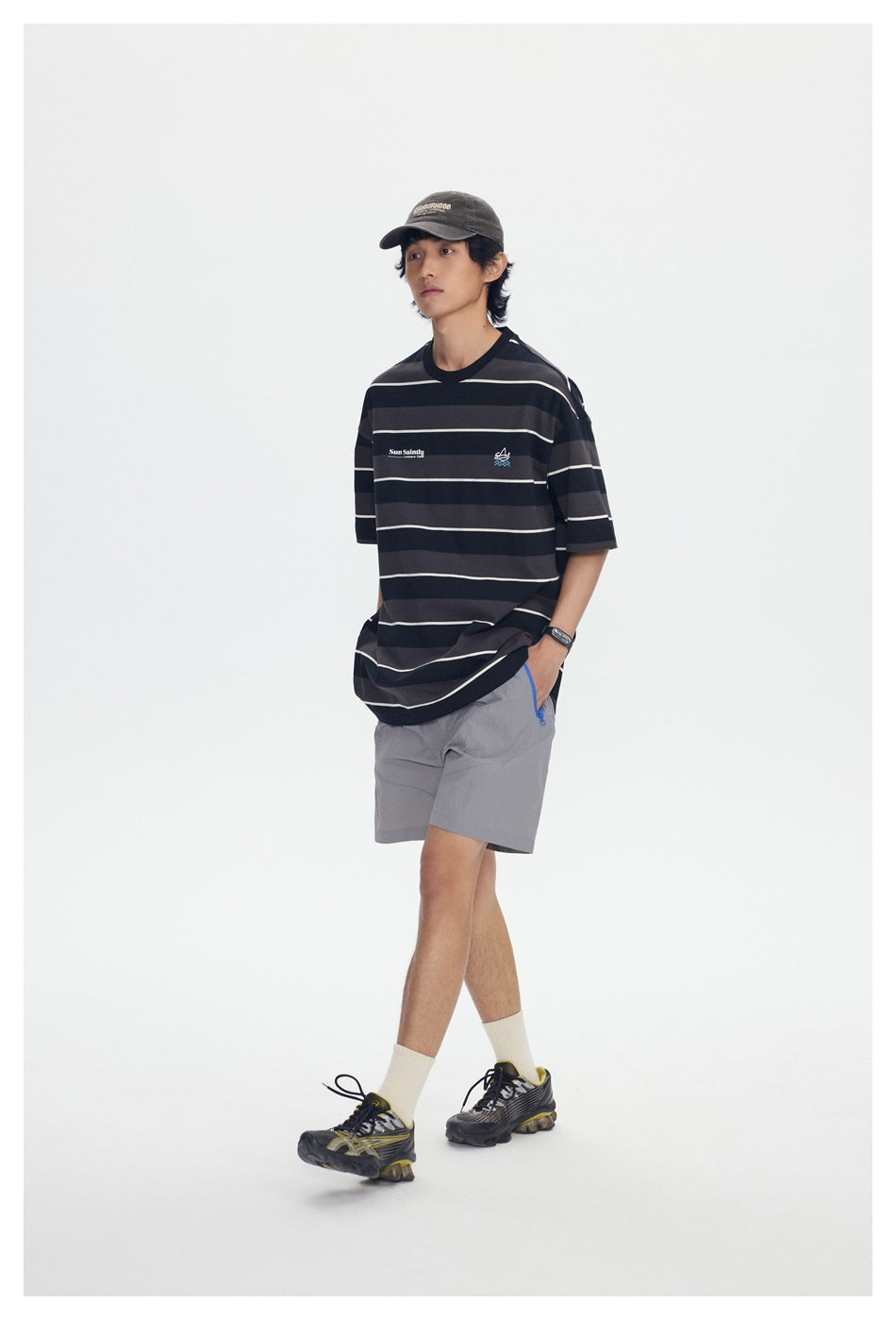Angled view of a model wearing an oversized black and charcoal striped T-shirt and gray shorts.