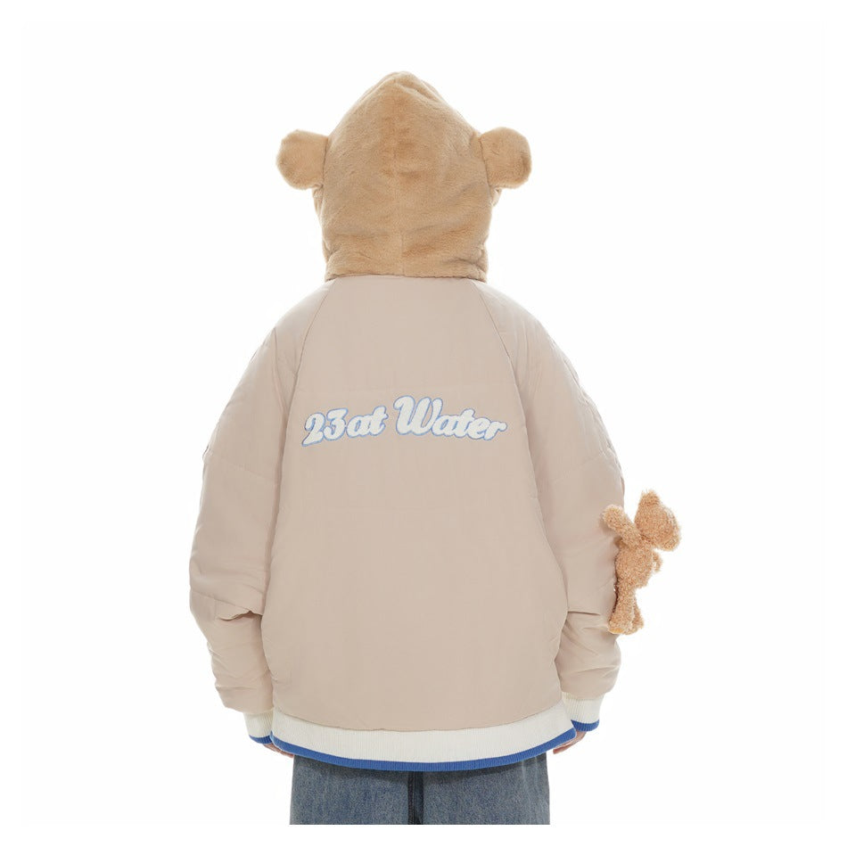 Back view of a person wearing a beige puffer jacket with a plush bear hood, blue-and-white trim and back lettering.