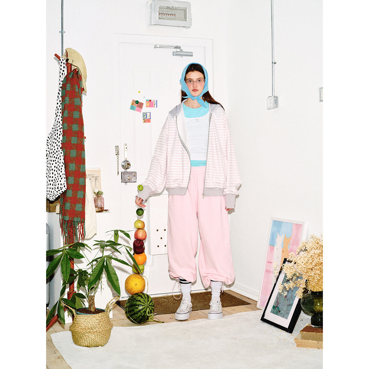 Front view of a model wearing an open pale pink-and-white striped zip hoodie with gray trim and loose pink pants.