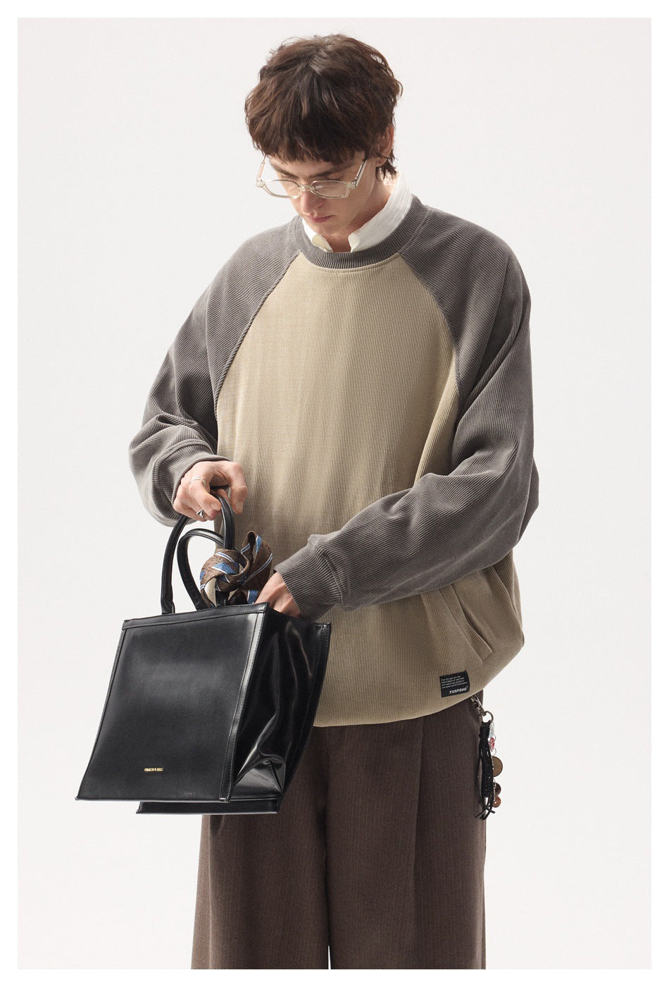 Front view of a model wearing a beige pullover with gray raglan sleeves and brown trousers.