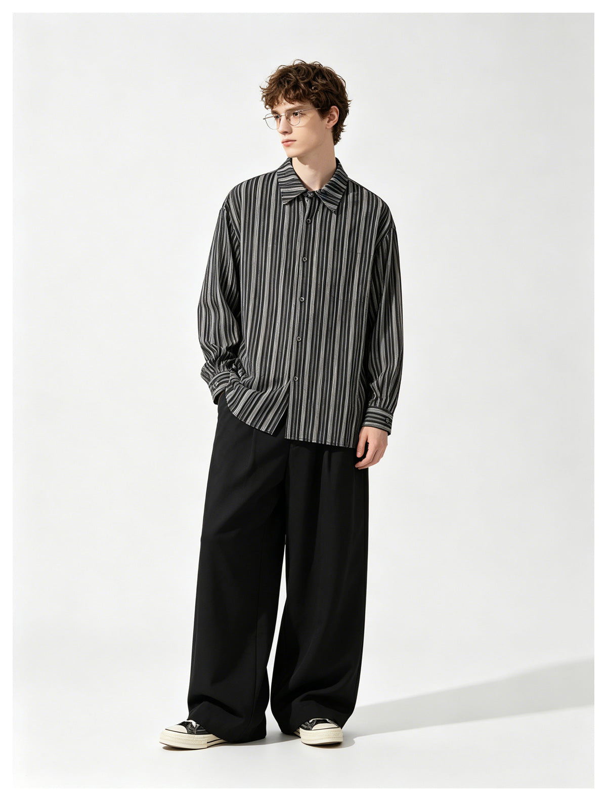 Model wearing a black and gray vertical-striped button-up shirt with wide black trousers and sneakers