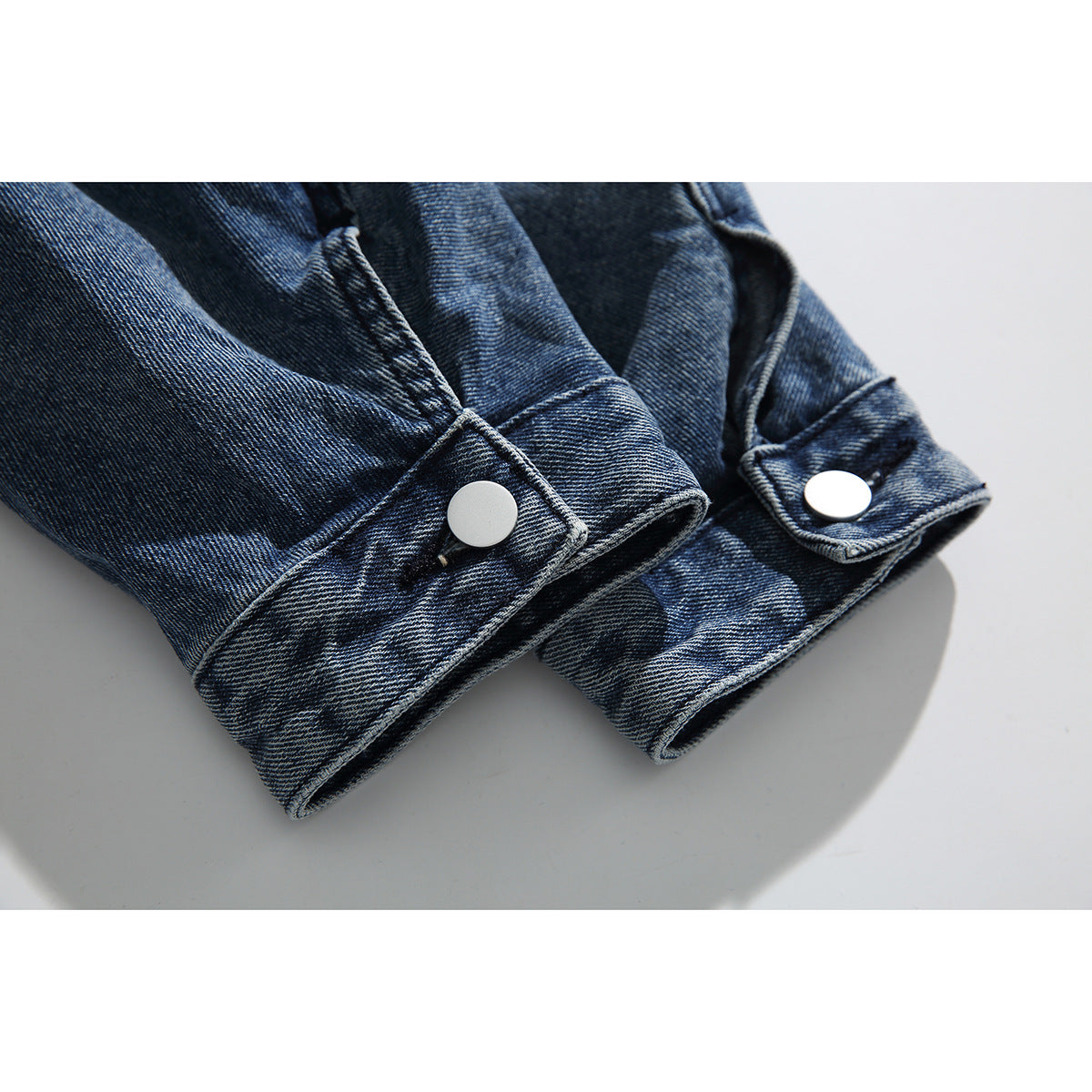 Close-up of washed blue denim jacket cuffs with silver snap buttons.