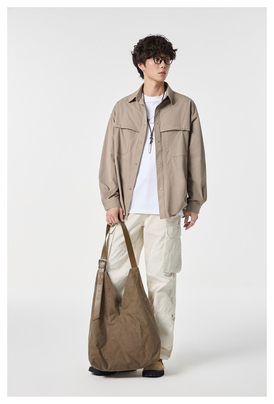 Full-length model wearing a taupe overshirt and cream cargo pants, carrying a large brown shoulder bag.