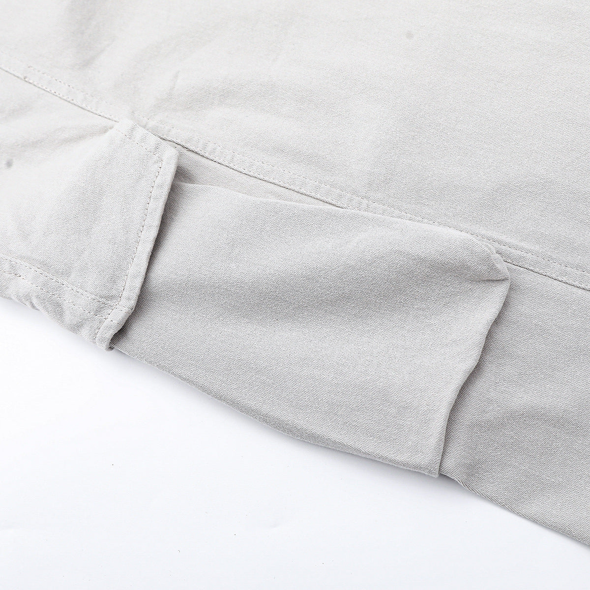 Close-up of light gray trousers showing a flap pocket and stitched seams.