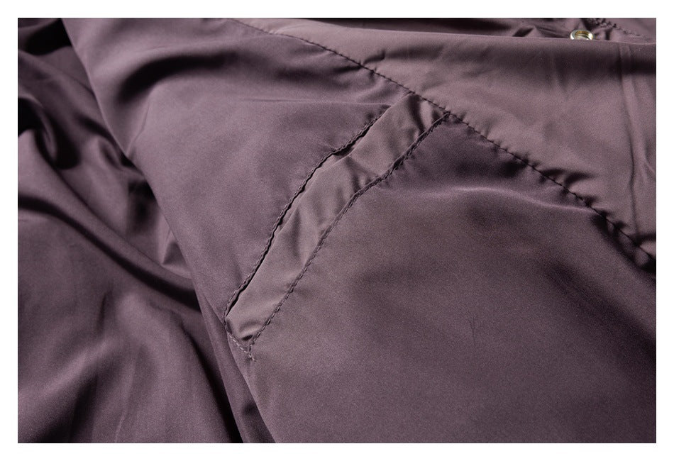 Close-up of a dusty mauve garment with a stitched pocket opening and a small metal snap near the edge.