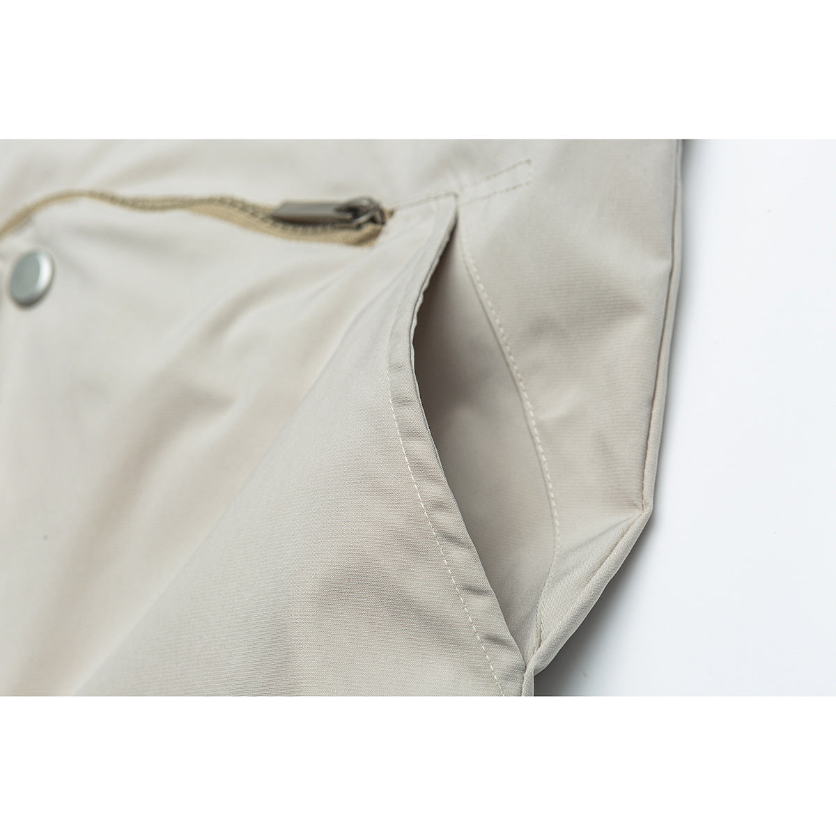 Close-up of a light beige jacket pocket opening with a zipper and snap detail.