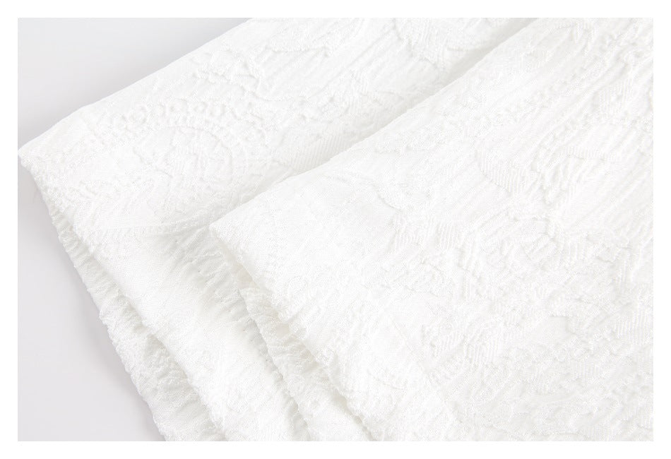 Close-up of folded white fabric showing a raised floral and geometric texture.