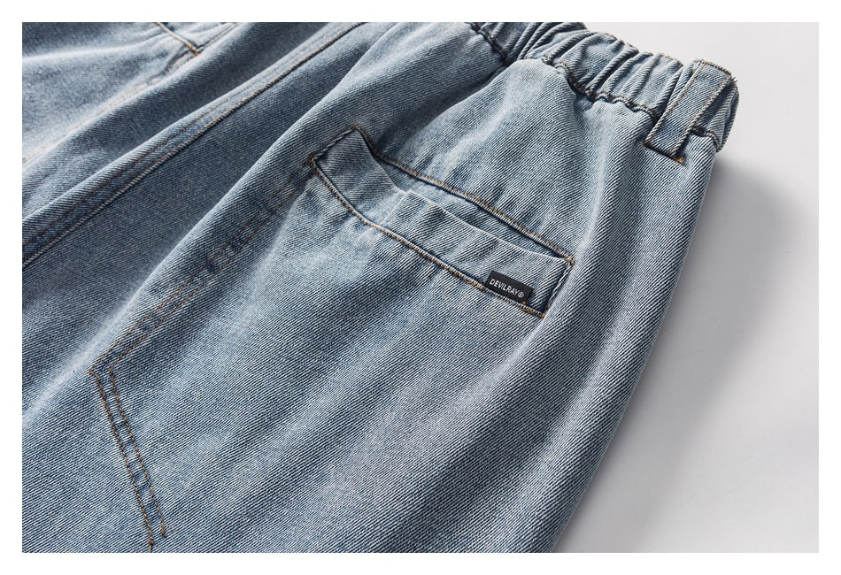Close-up of light blue washed denim pants showing an elastic waistband, belt loop, and rear pocket with a small black label.