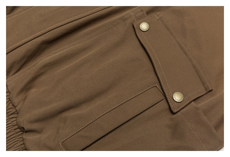 Close-up of brown trousers showing an elastic waistband, stitched pocket, and buttoned flap.