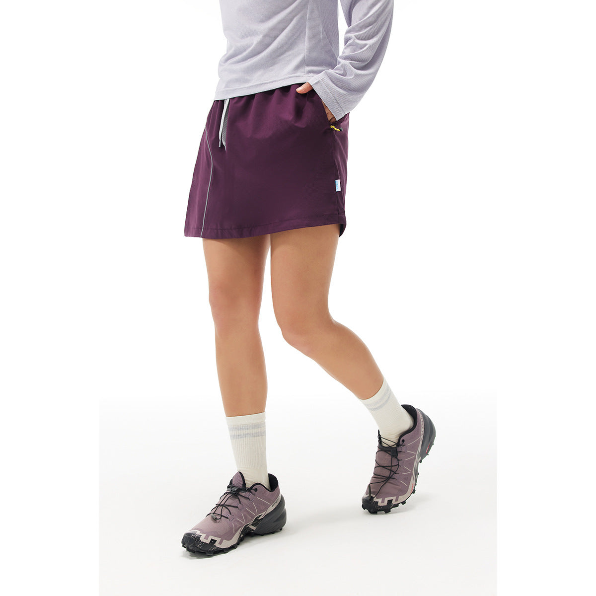Model wearing a plum athletic skort with a drawstring waist and zip pocket, shown from the front.
