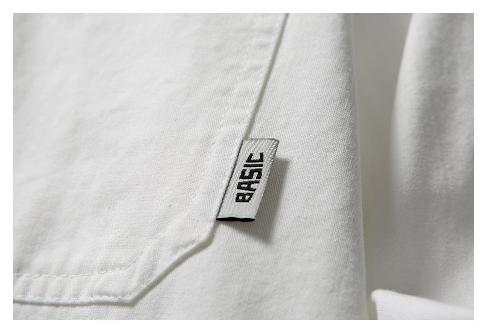 Close-up of a white garment with a small sewn label reading “BASIC” beside a stitched pocket edge.