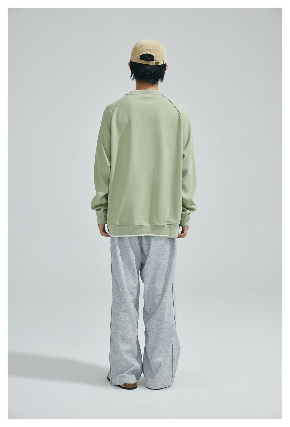 Rear view of a model wearing a plain sage green sweatshirt and loose gray pants.