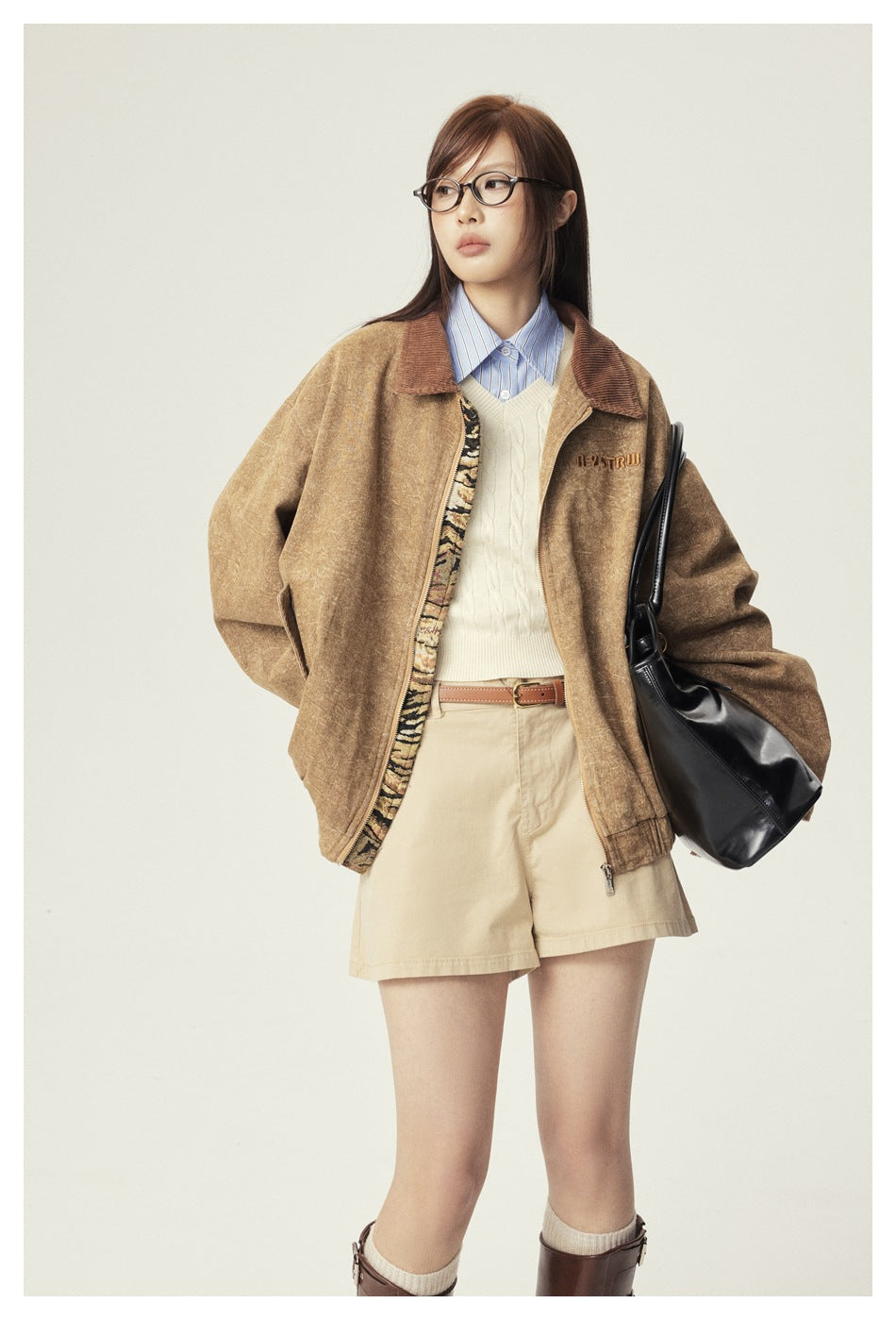 Model wearing a mottled tan zip jacket with a brown collar, styled with shorts, a sweater vest, and a striped shirt.