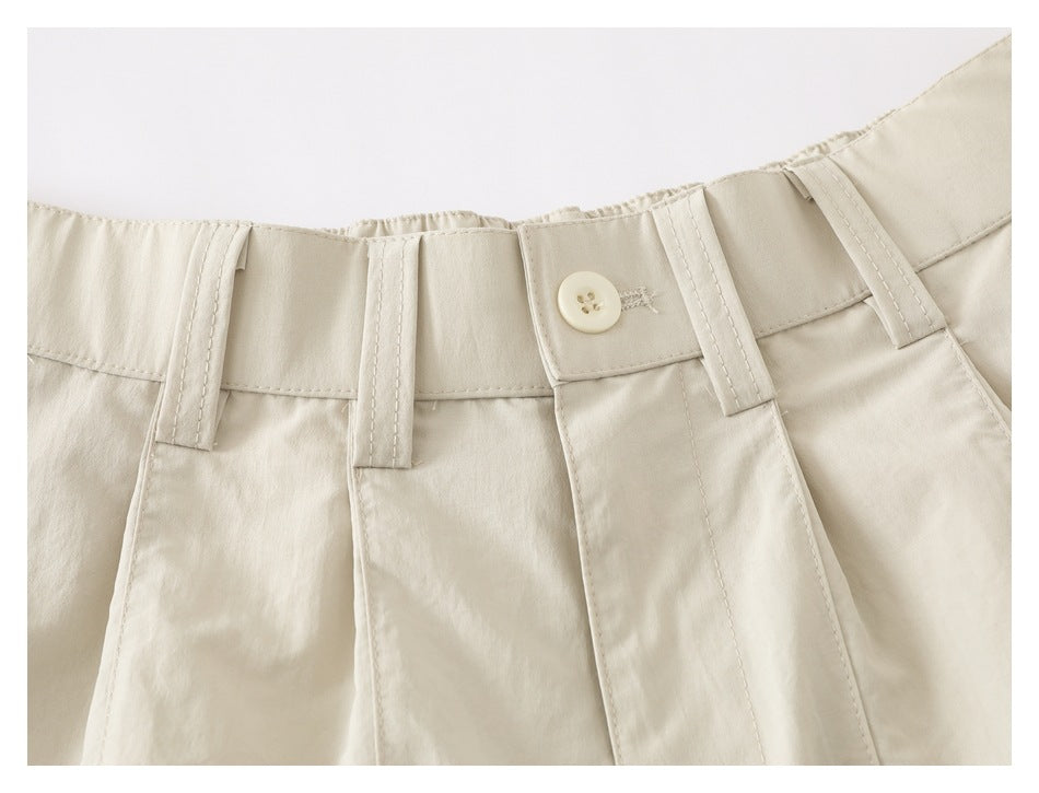 Close-up of the light beige shorts' waistband, belt loops, button closure, and stitching.
