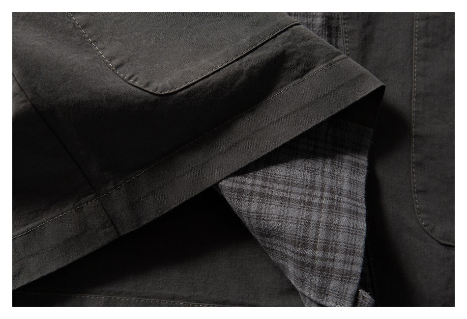 Close-up of a charcoal garment hem with gray plaid lining visible beneath the folded edge.