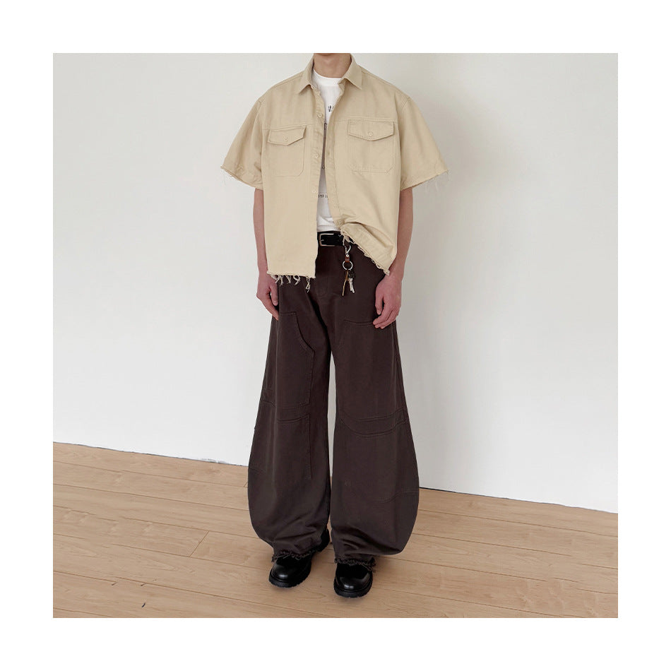 Model wearing a beige short-sleeve button-up shirt with two flap chest pockets and a frayed hem, paired with wide dark