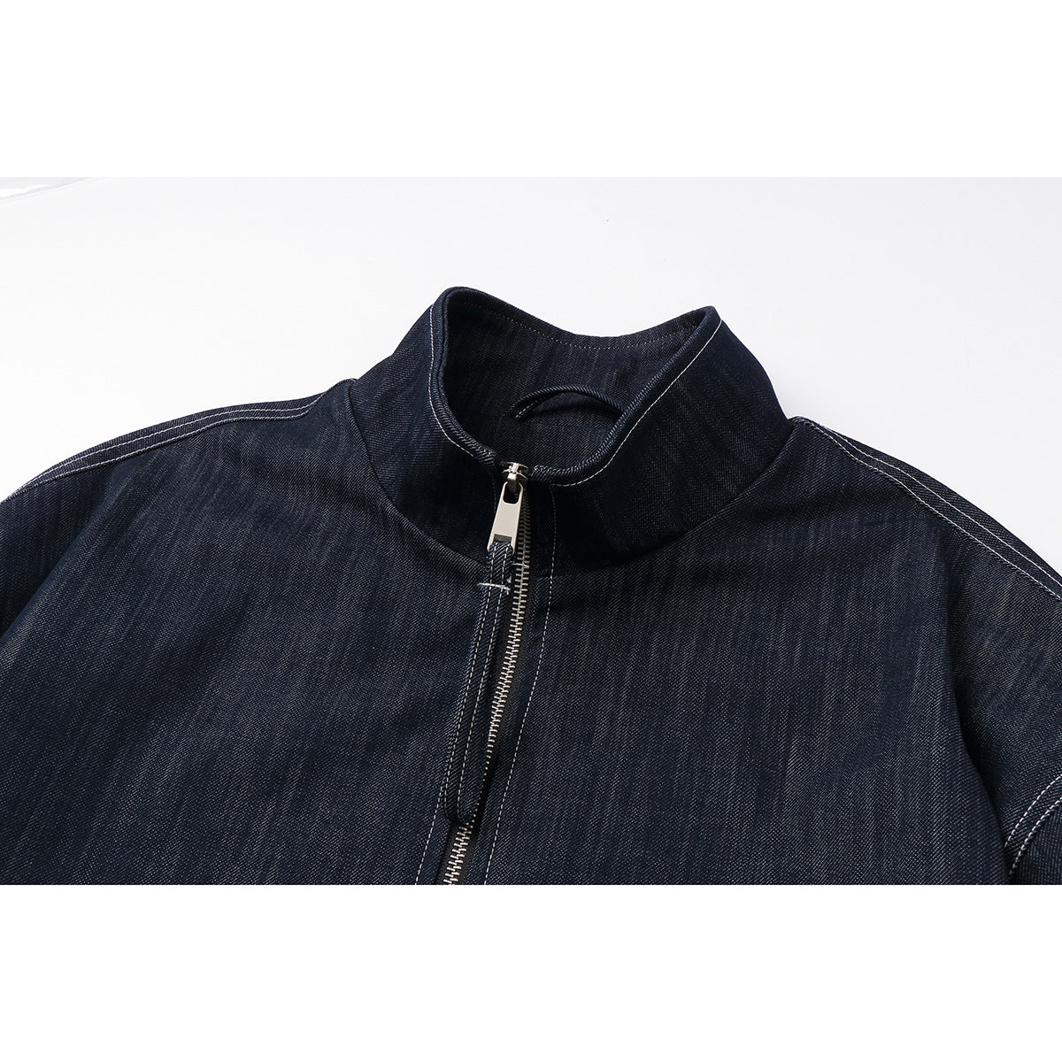 Close-up of a dark indigo jacket's stand collar, silver front zipper, and light contrast stitching.