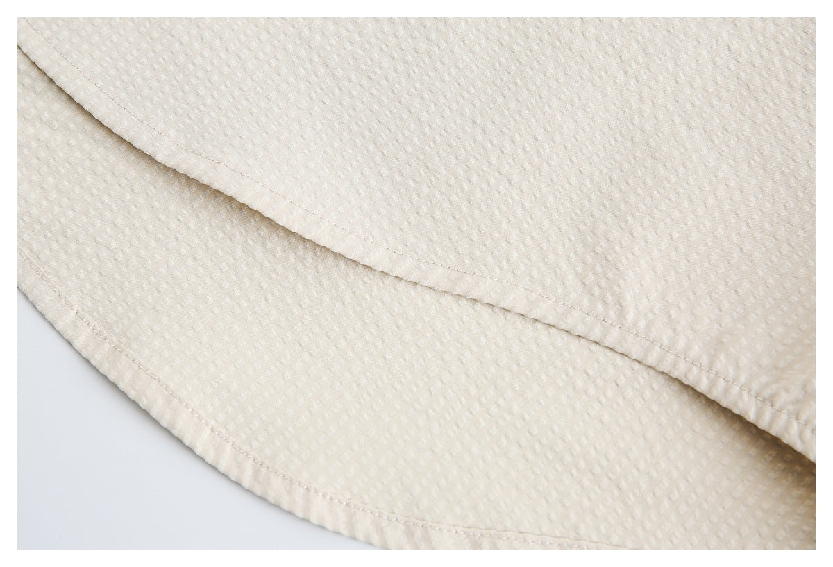 Close-up of the stitched curved hem on an off-white textured garment.