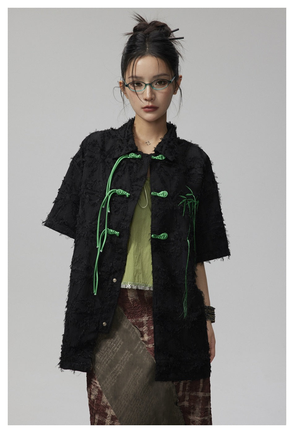Model wearing a black textured short-sleeve jacket with green frog closures and bamboo embroidery.