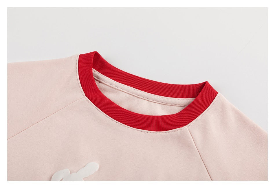 Close-up of the pale pink shirt's red ribbed crew neckline and shoulder seams.