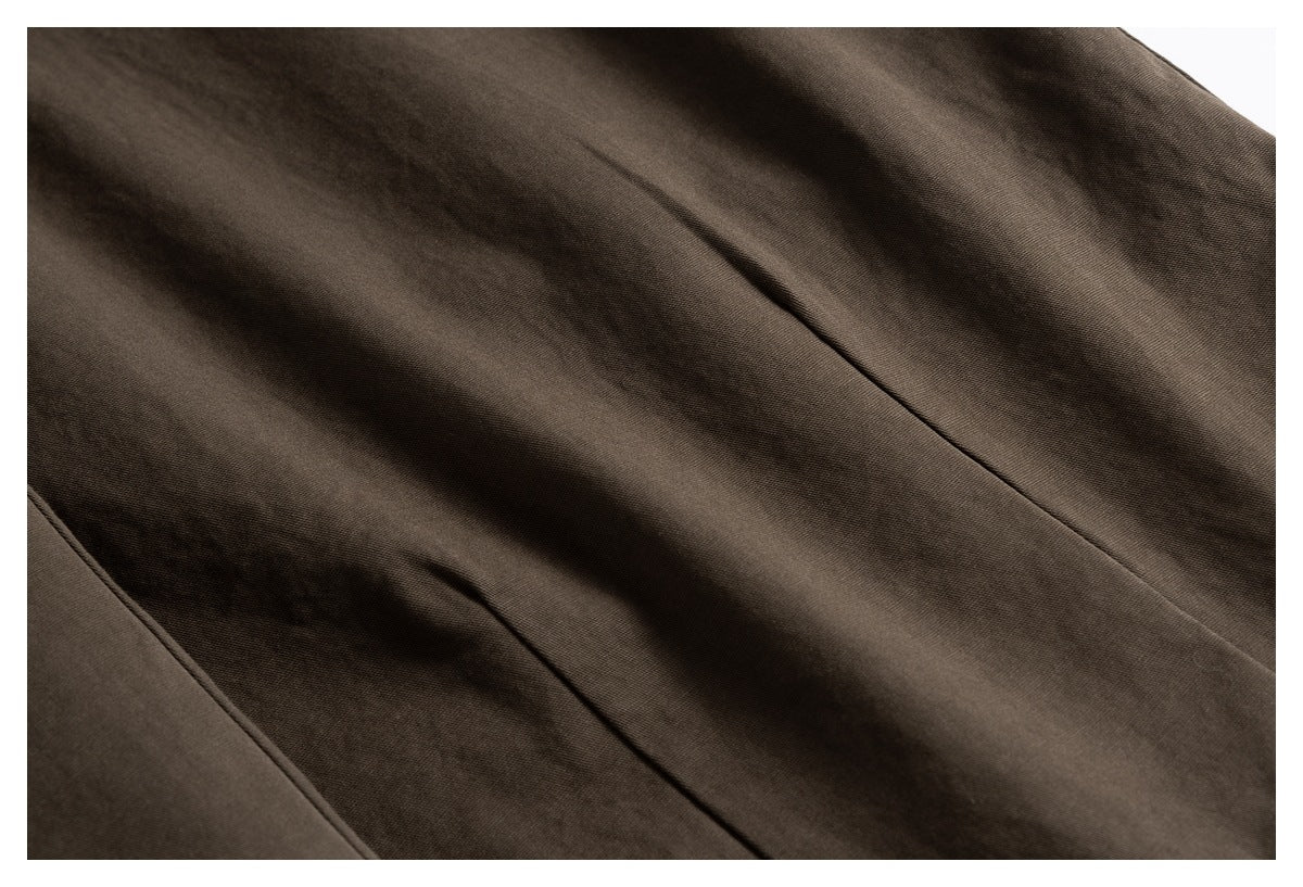 Close-up of dark brown trouser fabric with visible seams and soft folds.