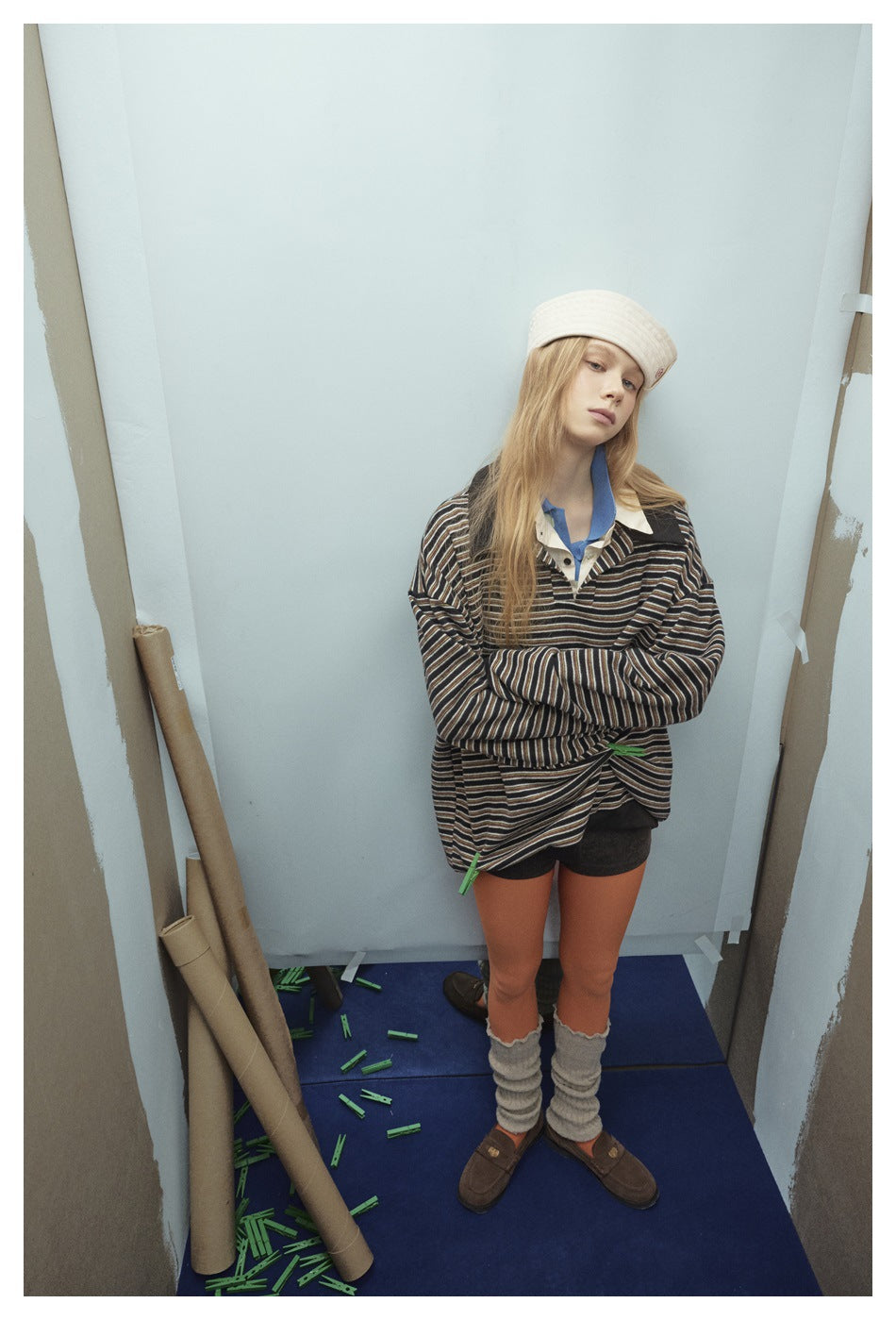 Model with arms crossed wearing an oversized striped polo-collar pullover over shorts and tights