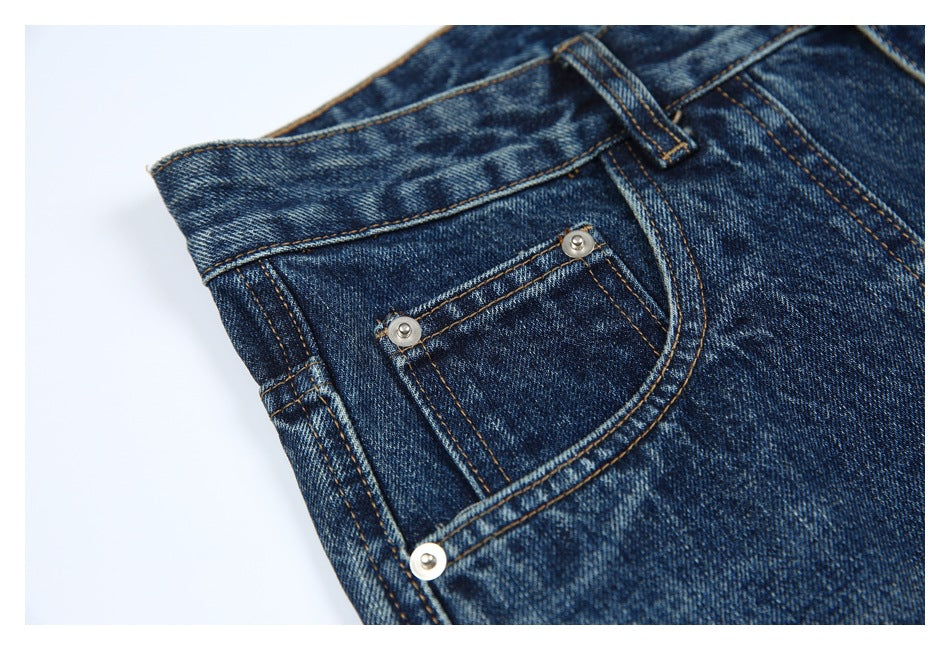 Close-up of dark blue faded jeans showing a curved front pocket, metal rivets and contrast stitching.