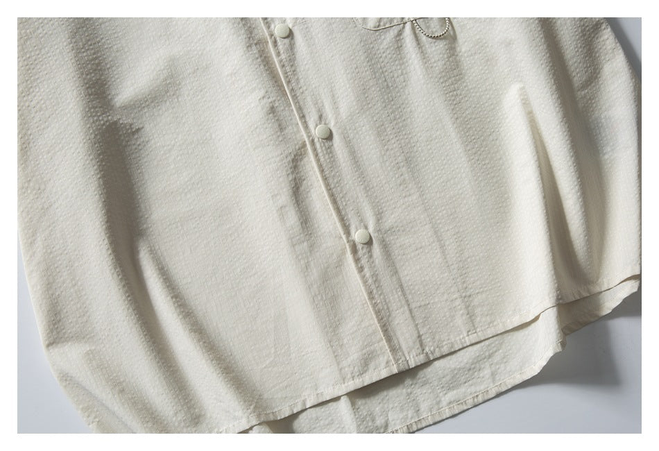 Flat-lay view of the ivory shirt's buttoned front, chest pocket, and curved hem.