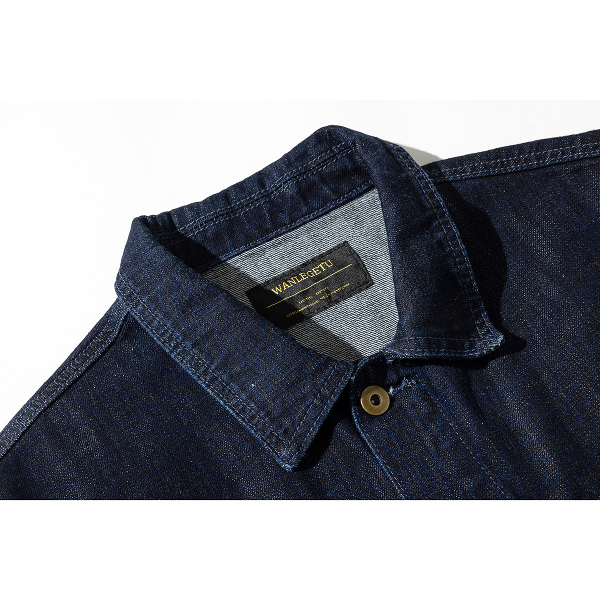 Close-up of a dark indigo denim jacket collar, showing a black-and-gold sewn label and brass button.