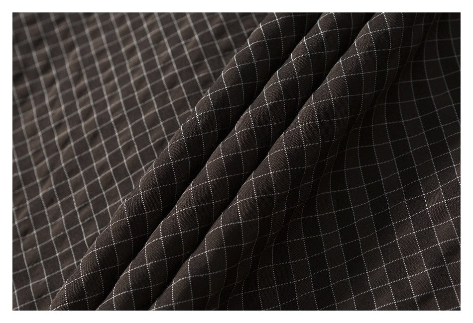 Close-up of dark brown fabric with a fine white windowpane grid, shown in soft folds.