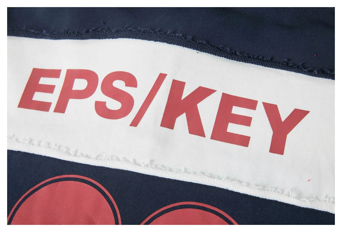 Close-up of red “EPS/KEY” lettering printed on a white garment panel between navy sections.