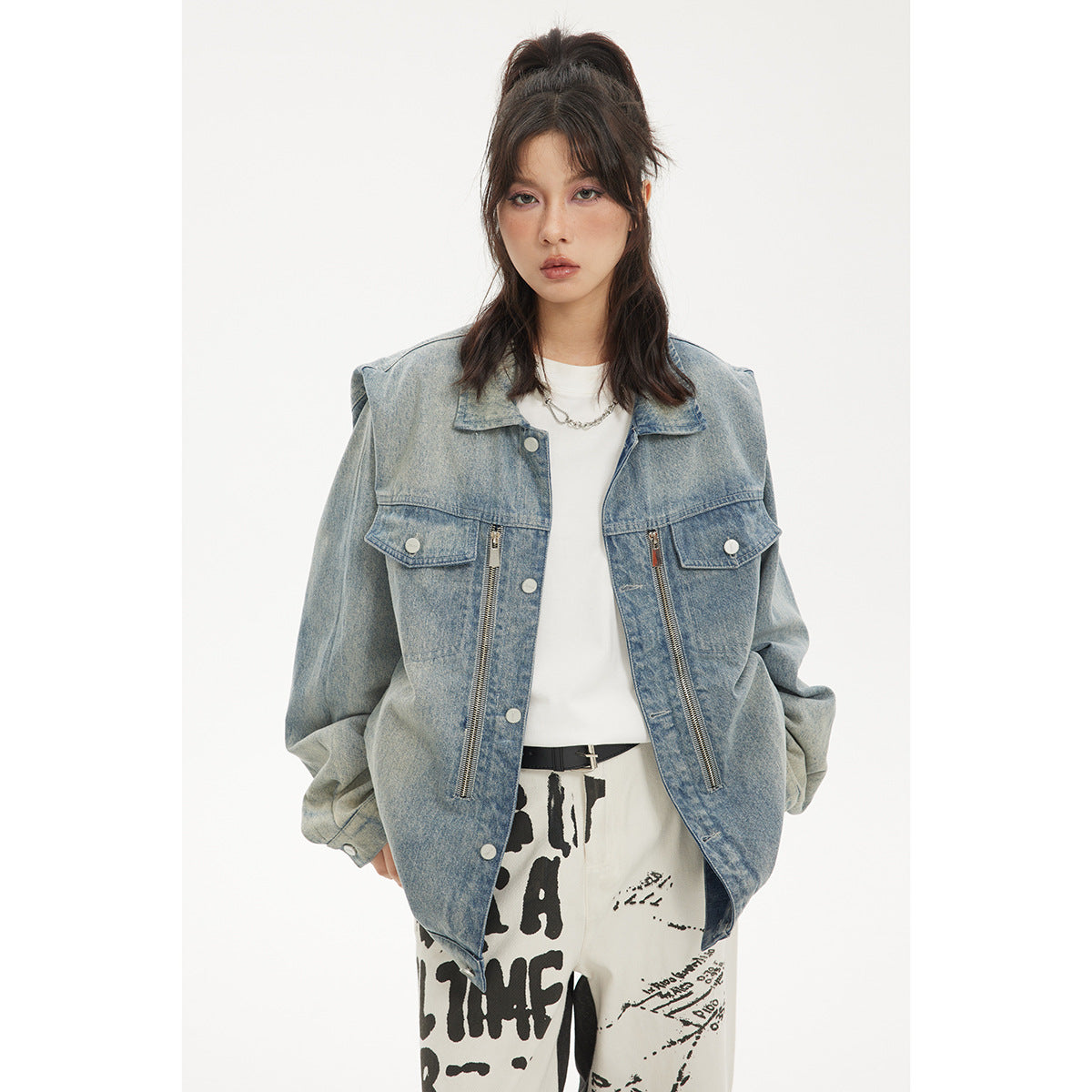 Front view of a model wearing an oversized faded blue denim jacket with flap pockets and long vertical zippers.