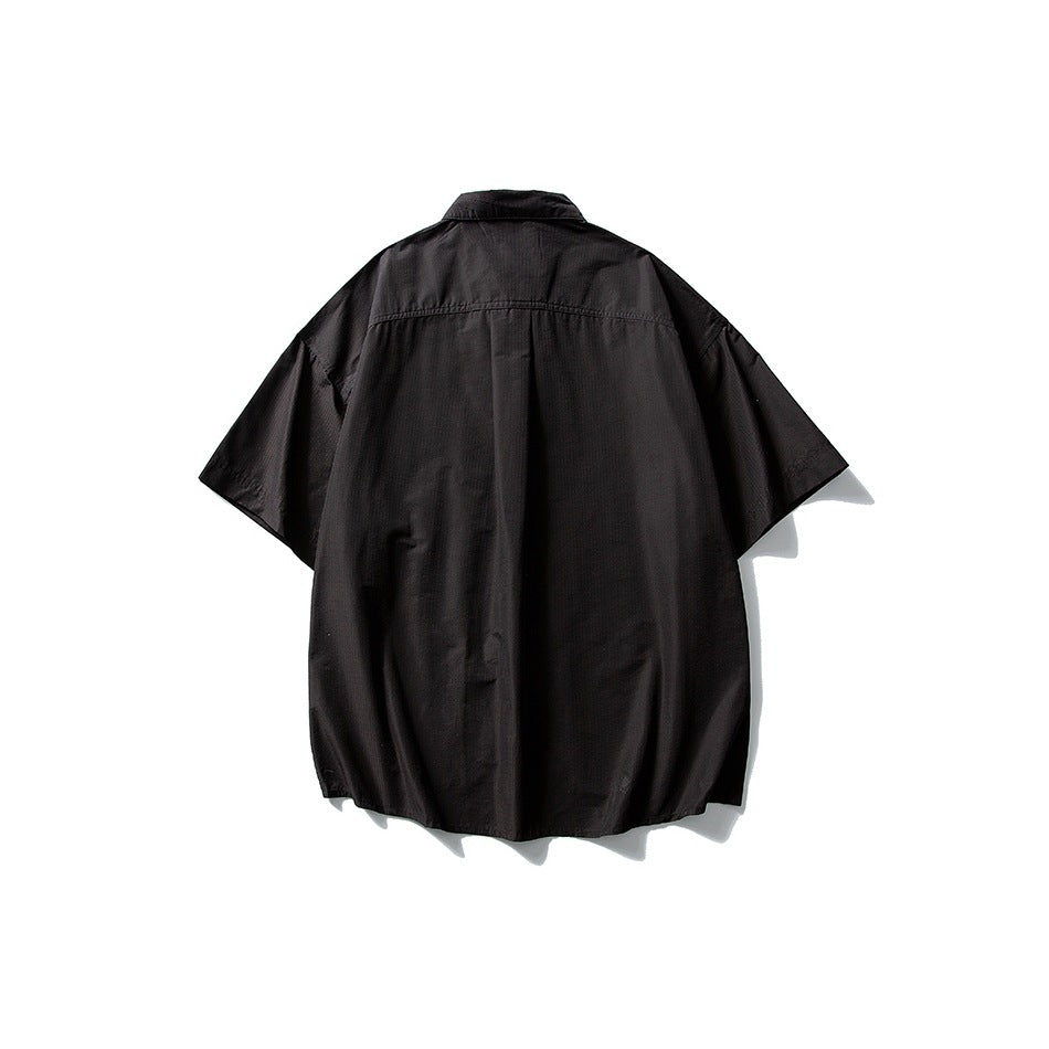 Back view of a black short-sleeve collared shirt with a center pleat and curved hem, displayed against white.