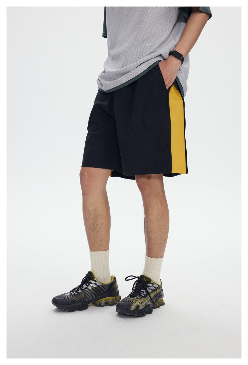 Angled close view of black shorts with a wide yellow side panel, worn with a light gray and dark green T-shirt.