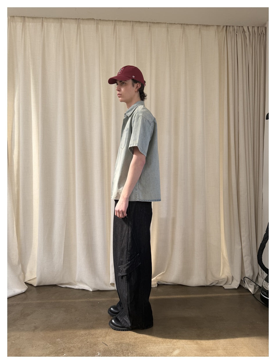 Side view of model wearing washed light blue short-sleeve shirt with black wide pants, boots and red cap