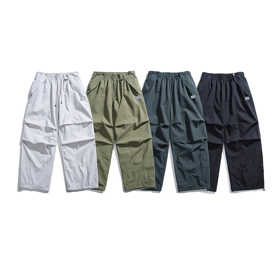 Four pairs of loose drawstring pants shown from the front in light gray, olive, blue-gray, and black.
