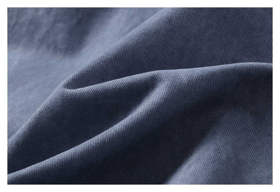 Macro close-up of the fine diagonal weave and folds of blue-gray trouser fabric.