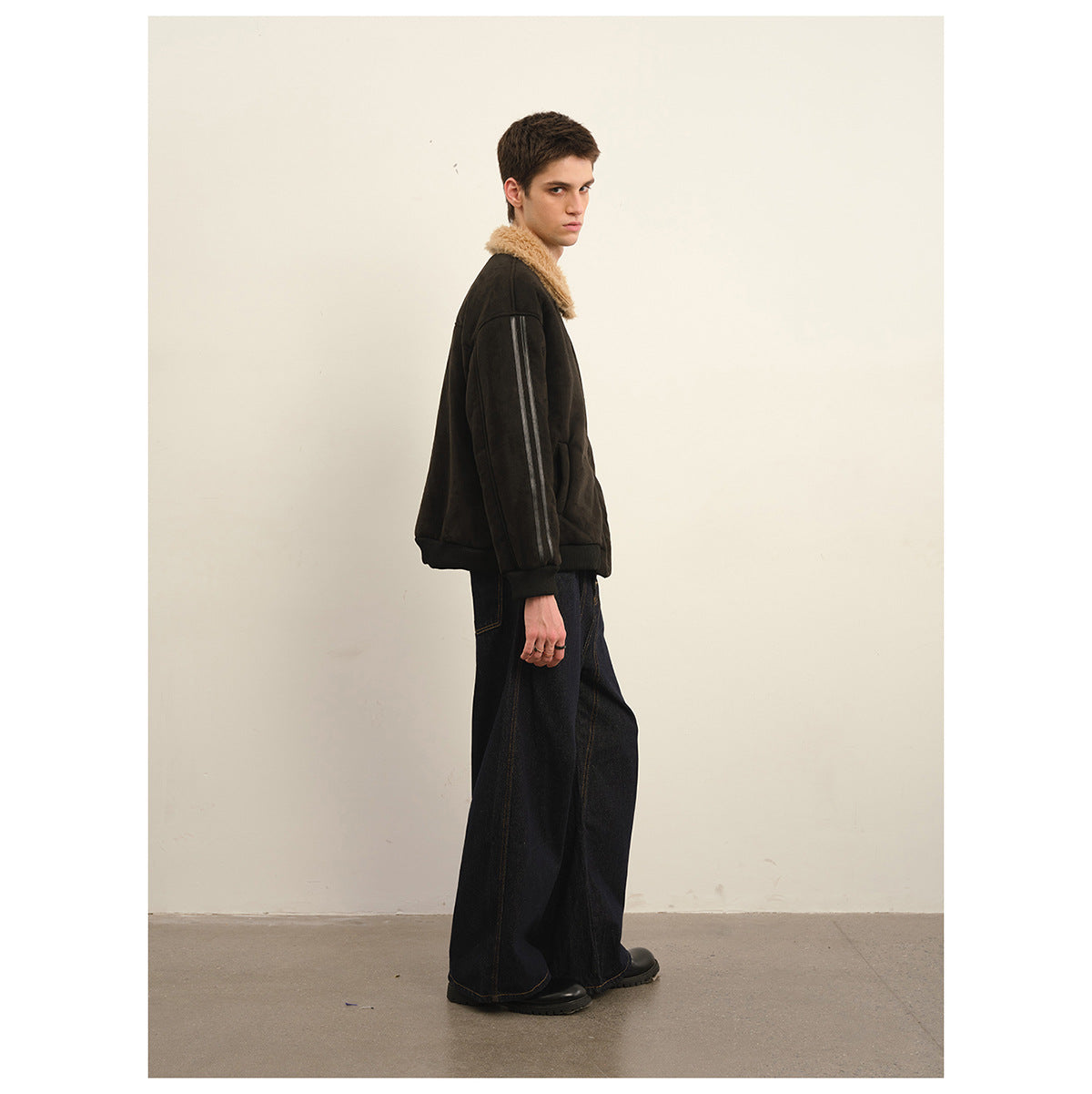 Side view of a model wearing a dark jacket with a tan shearling-style collar and striped sleeves.