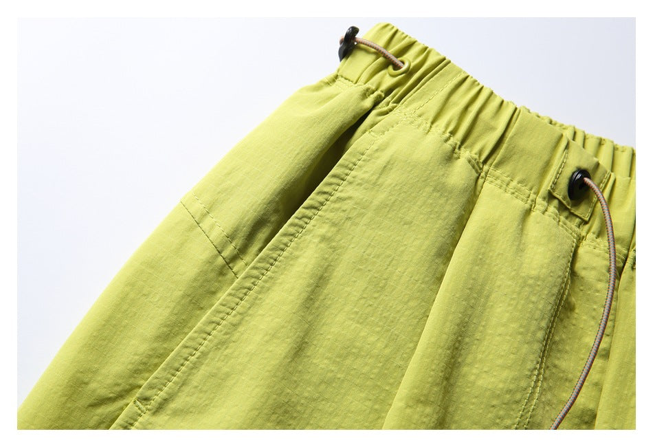 Close-up of yellow-green pants showing a side pocket seam, gathered waistband and adjustable drawcords.