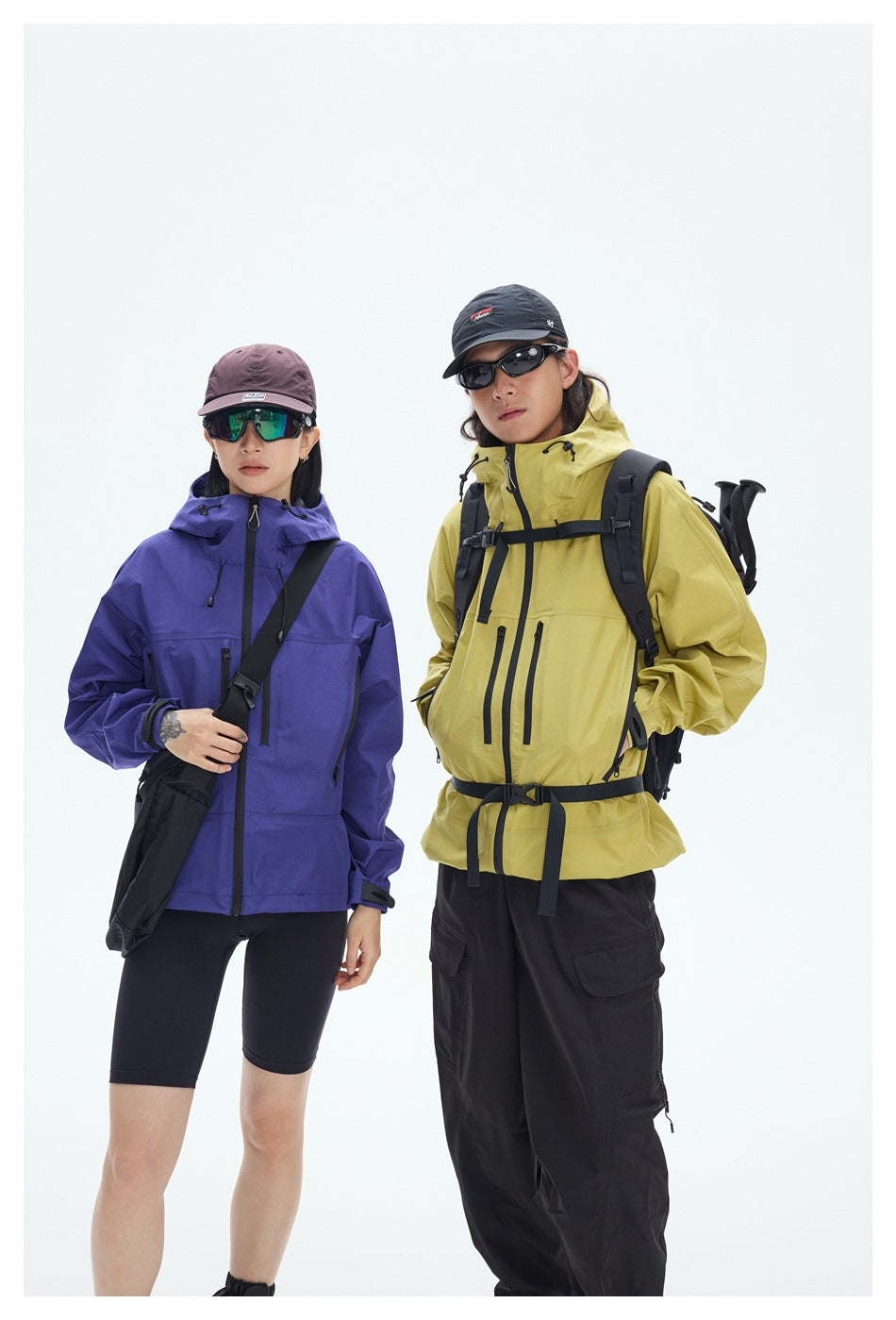Front view of two hikers in purple and yellow hooded jackets with black hiking pants and accessories.